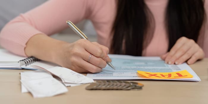A woman is focused on completing tax forms, using a pen and calculator to ensure accuracy in her financial planning.