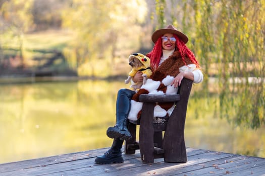 Autumn lake woman dog. She sits by a pond on a wooden pier in autumn and admires nature, holding a Yorkshire terrier in her hands. The concept of tourism, weekends outside the city