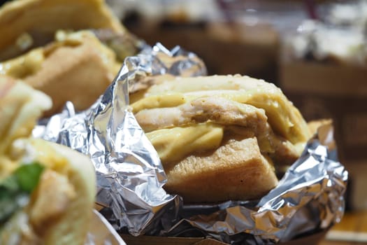 Tender chicken sandwich served in foil at a bustling food market.