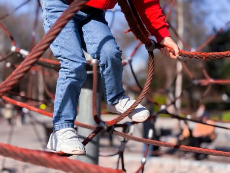 Child climbing on playground rope structure in park.