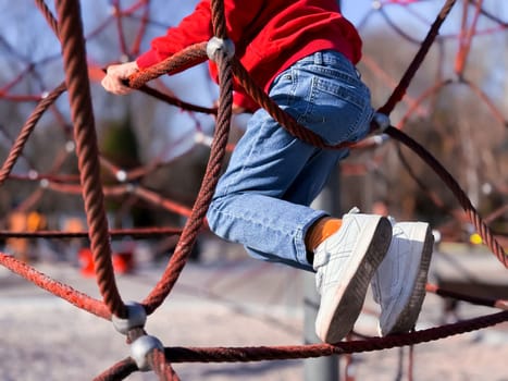 Child climbing on playground rope structure outdoors.