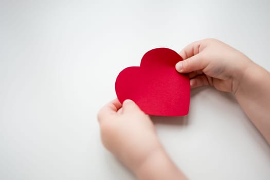 Child holding red heart shaped paper on white background.