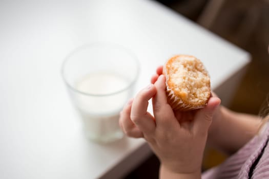 Child enjoying a muffin with a glass of milk at a table.