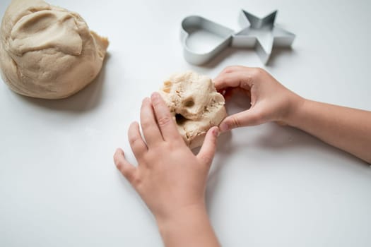 Child hands kneading dough with heart and star cookie cutters on white surface.