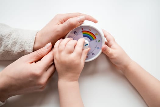 Caucasian adult and child hands interacting with colorful timer on white background.