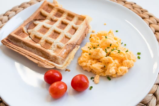 Breakfast plate with toast sandwich, scrambled eggs, and cherry tomatoes on white plate.