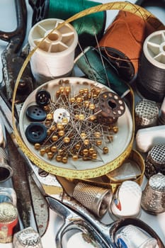 Sewing needles stuck in a green miniature spools thread Steel scissors, Spools of thread of various colour, Thimbles and Measuring tape including Pins and Buttons in small round tray. Sewing items set or Sewing objects (Sewing notions), use it as your Wallpaper, Poster and Copy space, Selective focus.