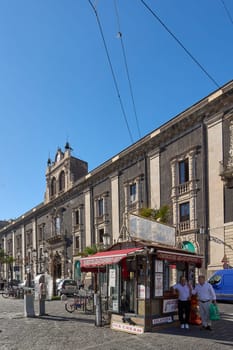 Catania. Italy - March 3, 2025: Majestic Palazzo Tezzano facade showcasing detailed design in Catania lively square. Captures daily life with pedestrians, a small caf and vehicles against a bright.