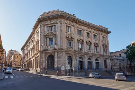 Catania. Italy - March 3, 2025: Stunning Palazzo Della Borsa facade with detailed stonework in Catania's bustling area. Showcases vehicles, walkers, and bright daylight, great for cultural exploration