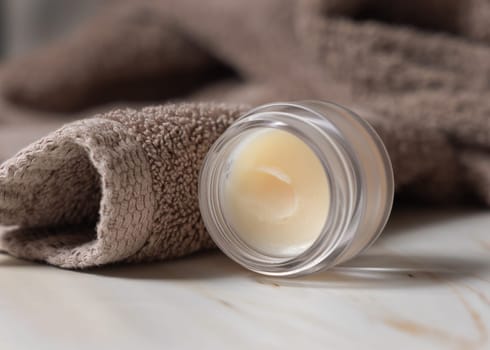Opened lip balm jar near light brown bath towel closeup, copy space. Herbal cosmetics for mens and woman daily lipcare and personal care