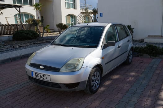Gaziveren Cyprus -01.03.2025 A silver hatchback sits in a sunlit courtyard, framed by greenery, evoking a calm seaside retreat vibe.
