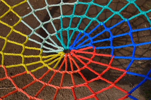 Brightly colored ropes form a spiral web, revealing stunning patterns against a textured ground in daylight.