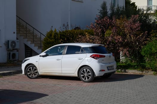 Gaziveren Cyprus -01.03.2025 A sleek white hatchback rests quietly against the backdrop of a contemporary structure surrounded by lush plants.