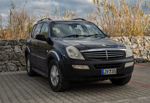 Gaziveren Cyprus -28.02.2025 A classic black SUV is parked on a paved area beside a rugged stone wall and tall greenery under cloudy skies.