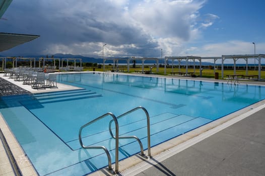 Bright blue waters await sunbathers at the quiet resort pool under a radiant sky and distant mountains.