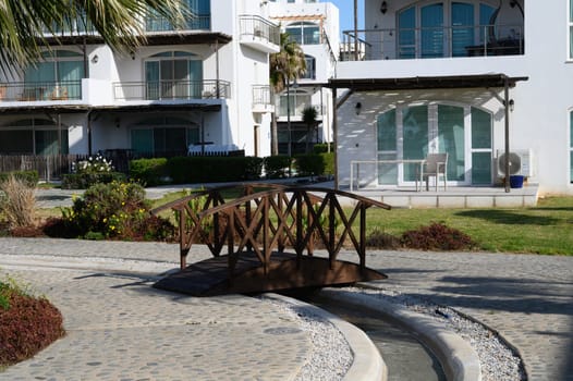 A serene bridge arches over a winding path, surrounded by lush greenery and elegant coastal architecture.