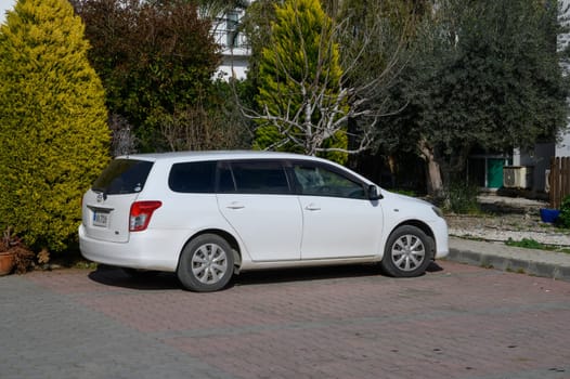 Gaziveren Cyprus -01.03.2025 A white station wagon rests beside vibrant shrubbery in a serene, sunlit residential area.