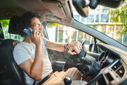 Man with curly hair and sunglasses, drives a car,smokes a cigarette and using phone.