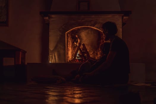 Family bonding by the fireplace during cozy winter evening. Warm and peaceful family moment indoors. Togetherness, love, and relaxation concept. A warm and inviting scene featuring a lit fireplace with glowing firewood and candles. A colorful traditional rug and pillow lie on the floor, creating a cozy atmosphere. Home, relaxation, and rustic comfort concept.