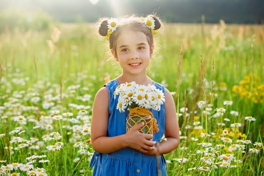 Adorable little girl holds a bouquet of daisies in a field with daisies on a sunny day. Copy space