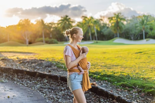 A loving mother walks through a peaceful park, carrying her baby securely in a sling. A heartwarming moment of maternal bonding, babywearing, and the joy of motherhood in nature.