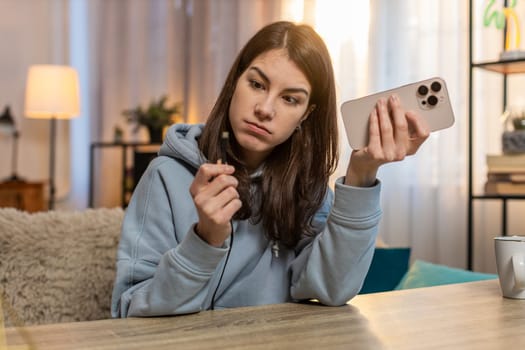 Young frustrated woman plugging charging cable into smartphone and unplugging it repeatedly as charger fails to work. Girl appears frustrated noticing cable is broken and unable to charge device.
