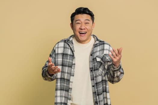 Asian middle-aged man pointing finger to camera, laughing out loud, taunting making fun of ridiculous appearance, funny joke anecdote, bullying, abuse. Adult Chinese guy isolated on beige background
