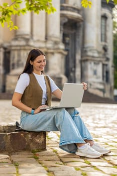 Caucasian woman freelancer working online distant job with laptop sitting on city street browsing website chatting outdoors during break. Girl looking at notebook screen send messages watching movies.