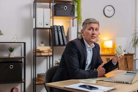 Poor Caucasian young businessman freelancer counting dollar cash insufficient amount of money. Financial crisis. Bankruptcy. Poverty and destitution. Male guy with laptop sitting at home office table.