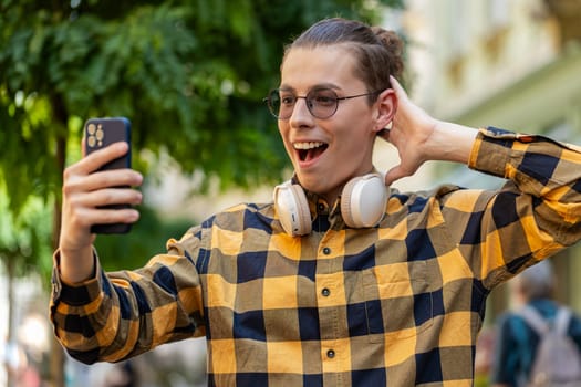 Happy Caucasian man using mobile smartphone celebrating win good message news, lottery casino app jackpot victory, online outdoors. Young male tourist freelancer stands on city street. Business people