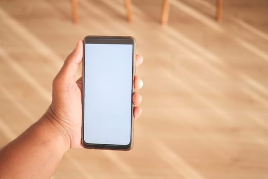 A person holds a smartphone with a blank screen in a bright room.