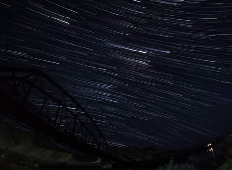 The night sky is filled with stars and the bridge is visible in the background. The stars are scattered throughout the sky, creating a sense of wonder and awe. The bridge adds a sense of structure