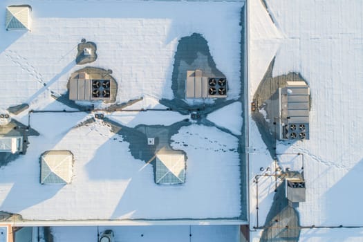 A roof covered in snow, with a few vents and chimneys visible. Scene is calm and peaceful, as the snow covers the roof and the vents and chimneys are barely visible