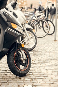 A row of scooters and bicycles parked on a cobblestone street in a European city. A perfect urban transportation concept for mobility, travel, and eco-friendly commuting projects