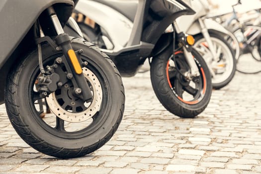 A close-up shot of scooter front wheels parked on a cobblestone street in a European city. A perfect urban mobility concept for transportation, eco-friendly travel, and city commuting projects