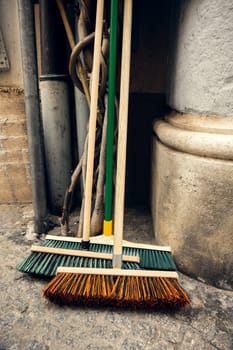 Wooden-handled brooms with colorful bristles leaning against a stone wall. Ideal for cleaning, urban maintenance, and sanitation concepts