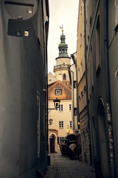 Narrow European alley with historic architecture and a church tower. A charming cobblestone alley in a historic European town, framed by old buildings leading to a church tower in the background