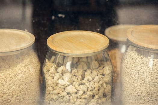 Glass jars with wooden lids filled with dry food in a rustic store. The reflection on the glass adds depth, emphasizing a sustainable and eco-friendly shopping concept