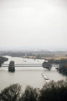 Cargo ship passing under a steel bridge on a river, aerial view. Rural and industrial landscape in the background. ideal for transport, trade, and logistics visuals