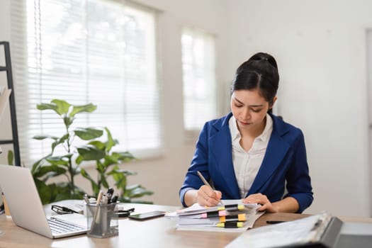 An accountant diligently writes notes while reviewing financial documents, demonstrating professionalism and attention to detail in her workspace.