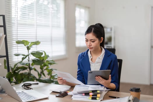 An accountant examines financial paperwork while using a tablet, showcasing organization and focus in a professional environment.