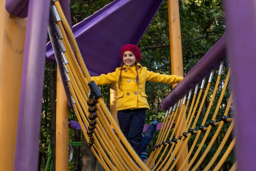 Happy little girl enjoying rope bridge in colorful park playground adventure.