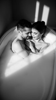 Monochrome image of a bathtub filled with foam. In the bathtub, a woman and a man in love are embracing. High quality photo