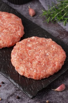 Fresh ground meat patty ready for cooking with herbs and garlic on a dark plate.