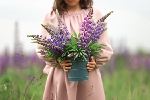 Young girl holding purple and blue lupine flowers in a field.