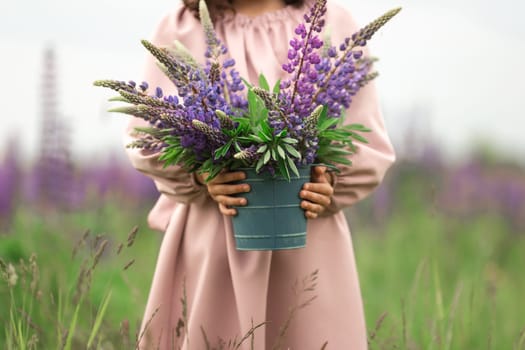 Young female holding lupine bouquet in flower field with pink dress.