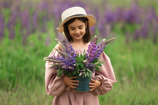 Smiling young caucasian girl holding lupine flowers in a meadow.