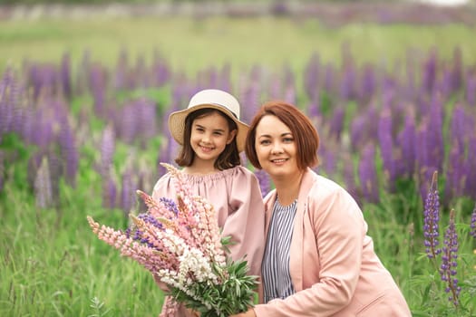 Caucasian woman and young girl smiling in a field of purple lupines on a sunny day.