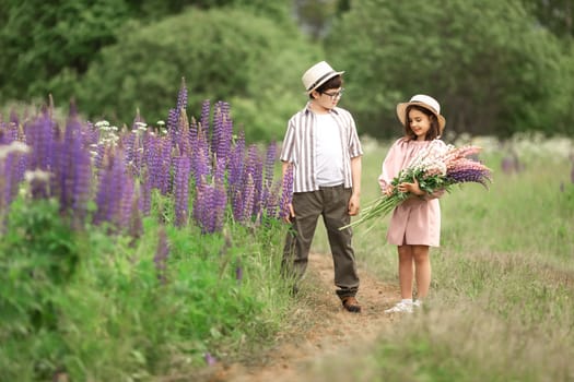 Caucasian children in flower field: boy and girl with hats and bouquet of lupines.