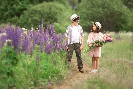 Caucasian children in summer field holding flowers and wearing hats.
